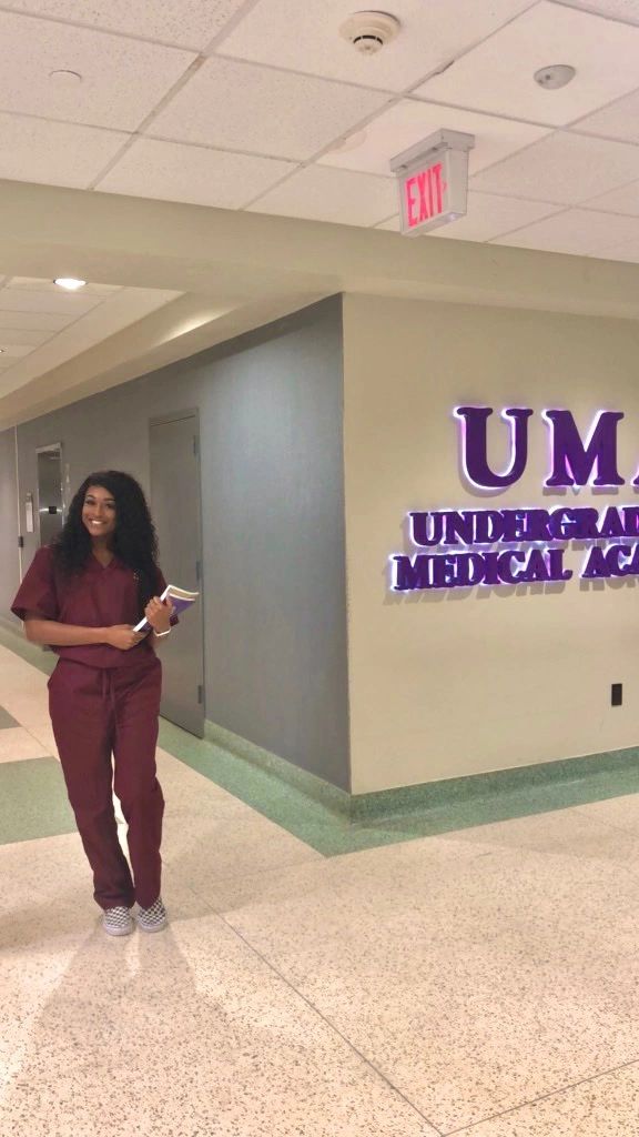Student in burgundy scrubs standing in a university hallway
